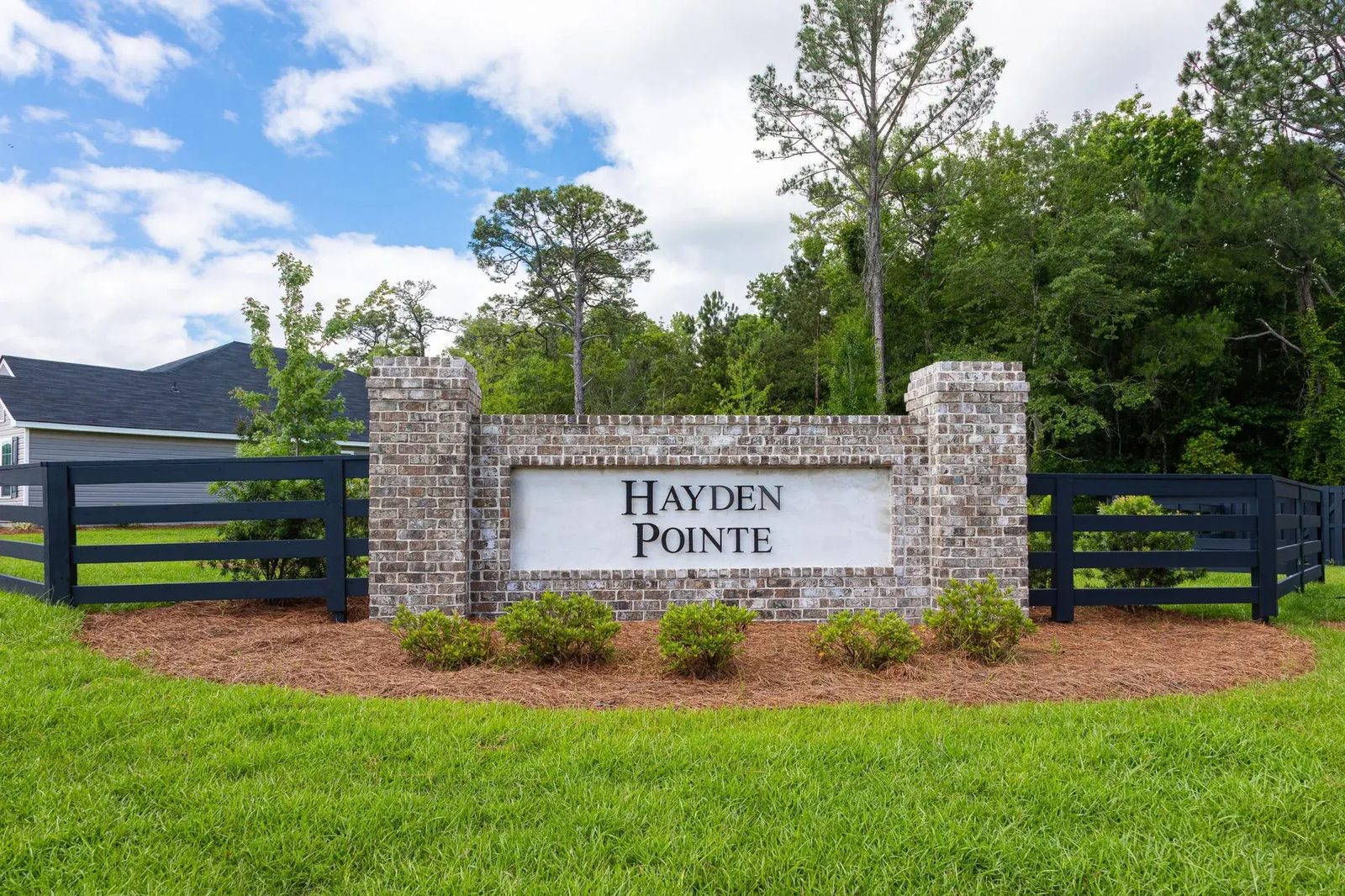Hayden Pointe community entrance monument with brick columns, black ranch fencing, and a new-construction home beyond the lawn
