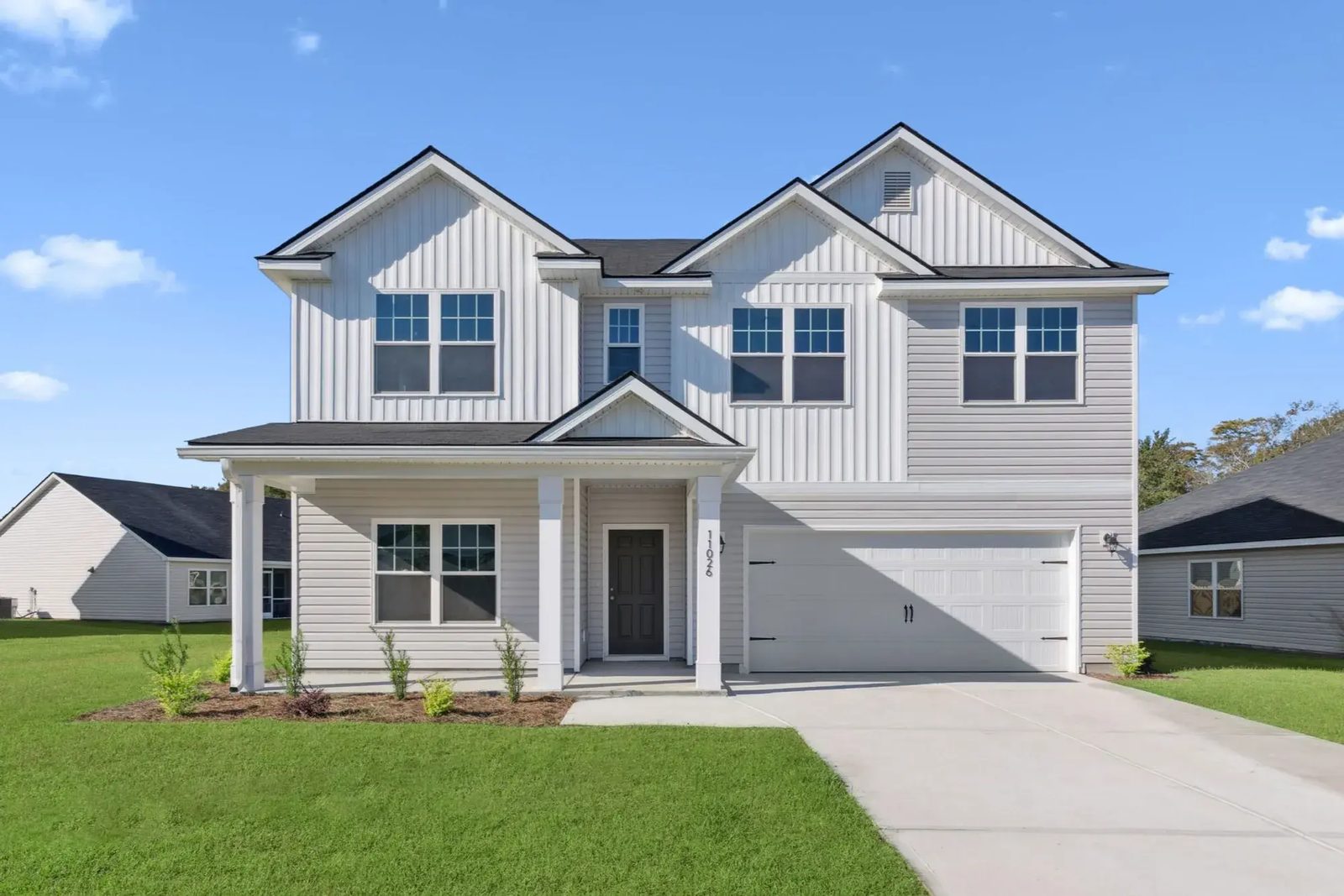 Two-story new-construction Smith Family Homes house at Sweetwater with board-and-batten gables, a covered front porch, and a two-car garage