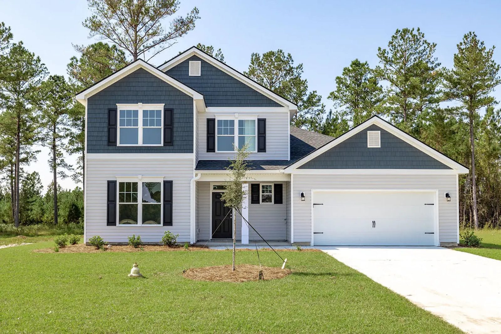 Two-story new-construction Smith Family Homes house at The Lakes with light gray siding, shake gables, a covered entry, and a two-car garage