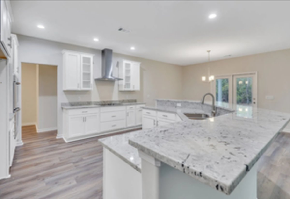Granite kitchen island with white shaker cabinetry, stainless steel appliances and a stainless steel vent hood, opening onto the breakfast area