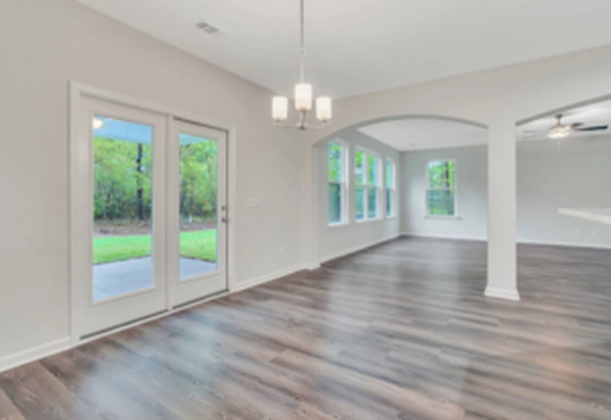 Open first-floor living area with French doors leading onto the covered back porch, LVP flooring and natural light through tall windows